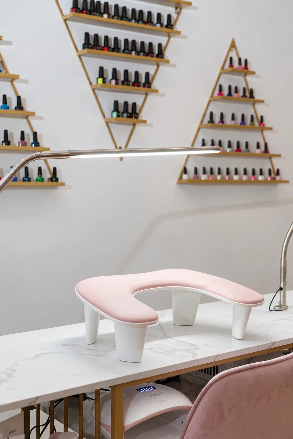 Rosa håndstøtte og farvehylder ved Nailtechs manicurebord